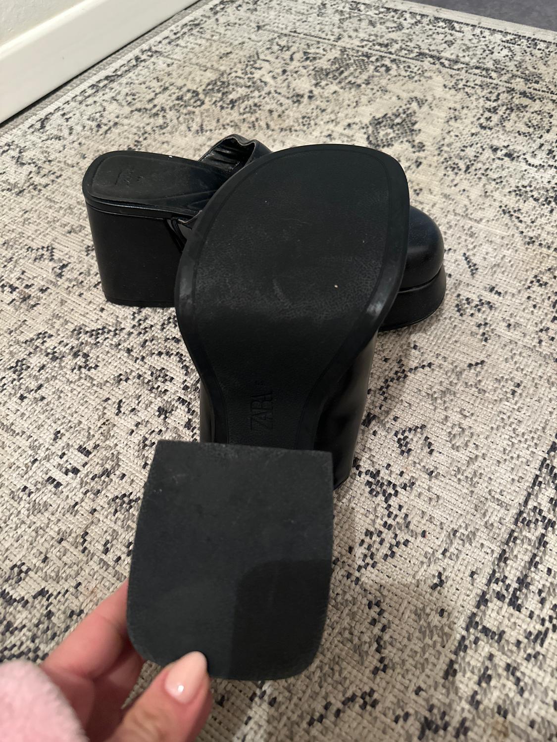 Black platform footwear on a textured grey carpet. A hand is holding an additional sole.