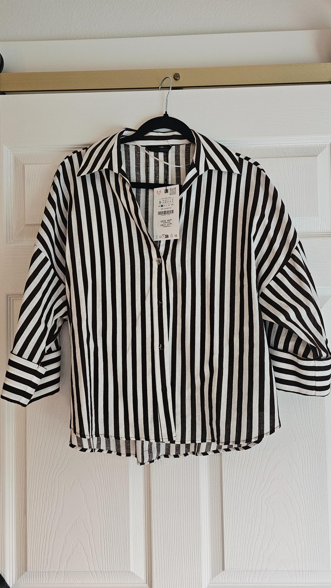 Black and white vertical striped shirt hanging on a black hanger over a white door. Label visible in the centre.