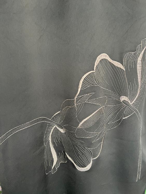 Gray fabric with white thread floral embroidery, displaying an elegant and detailed design on a plain background.