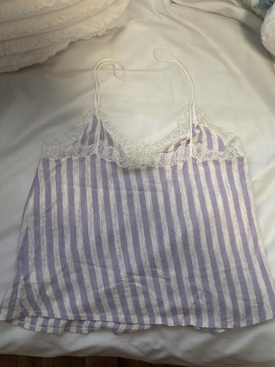 Tank top with lace on the neckline, purple and white vertical stripes, on a white bed.