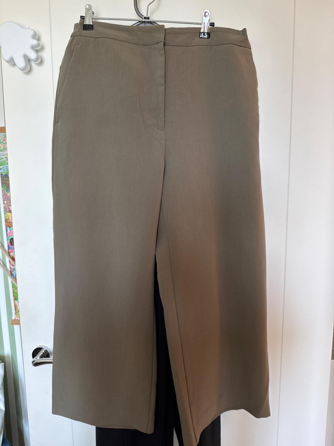 Beige trousers hanging on a hanger over a white door. Partially visible background with colourful details.