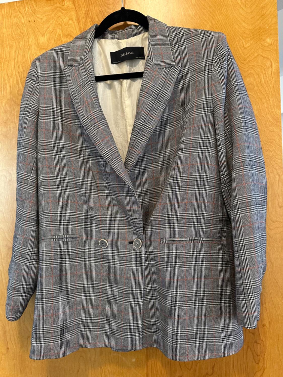 Front view of a grey checked blazer with side pockets and a double-breasted fastening.