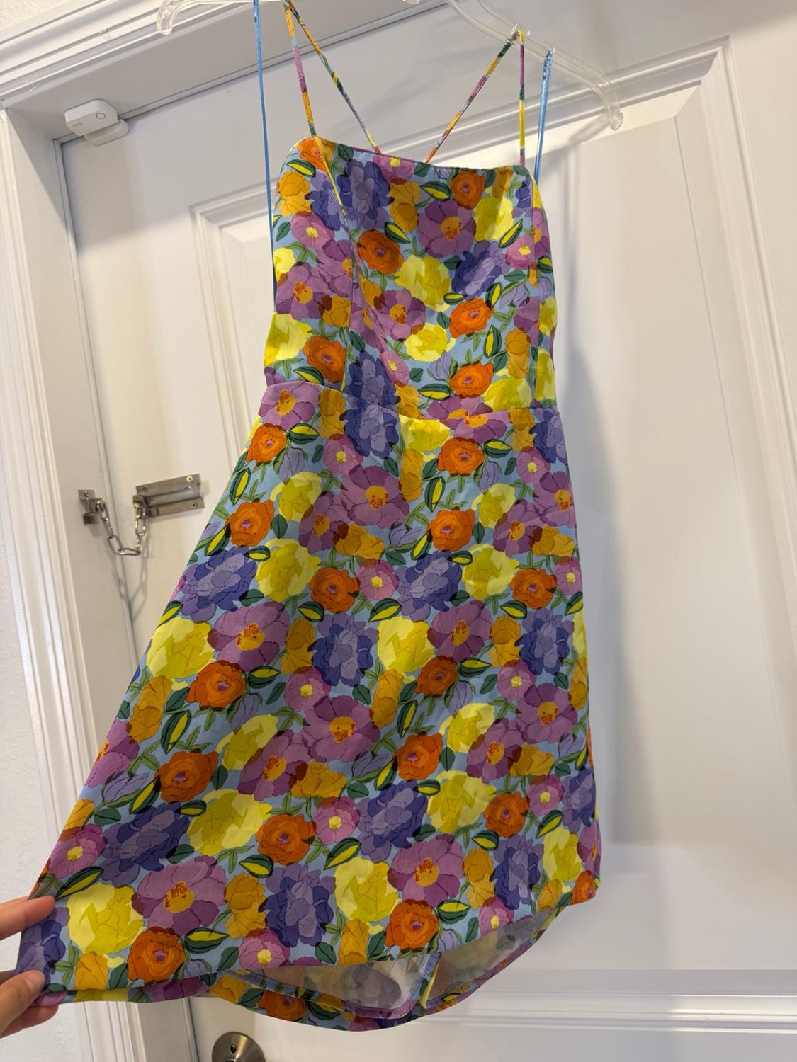 Purple, yellow and orange floral print strappy mini dress, hanging on a white door.