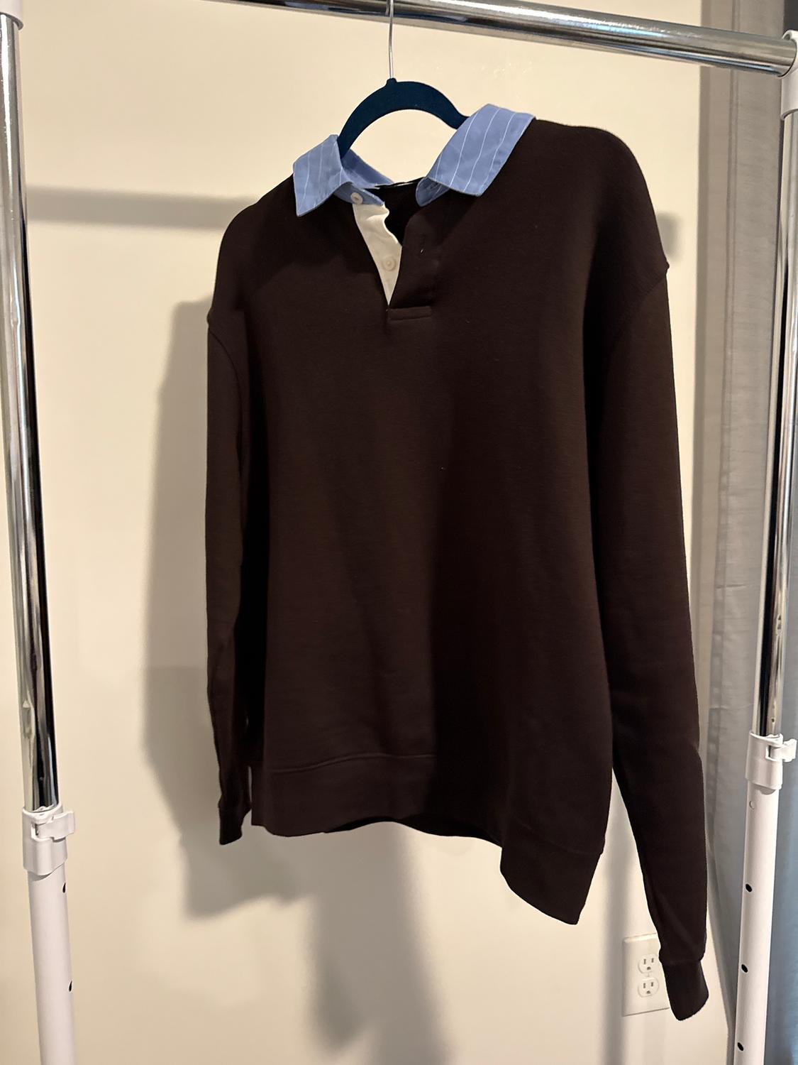 Brown jumper with light blue and white shirt collar, hanging on a blue hanger on a metal stand.