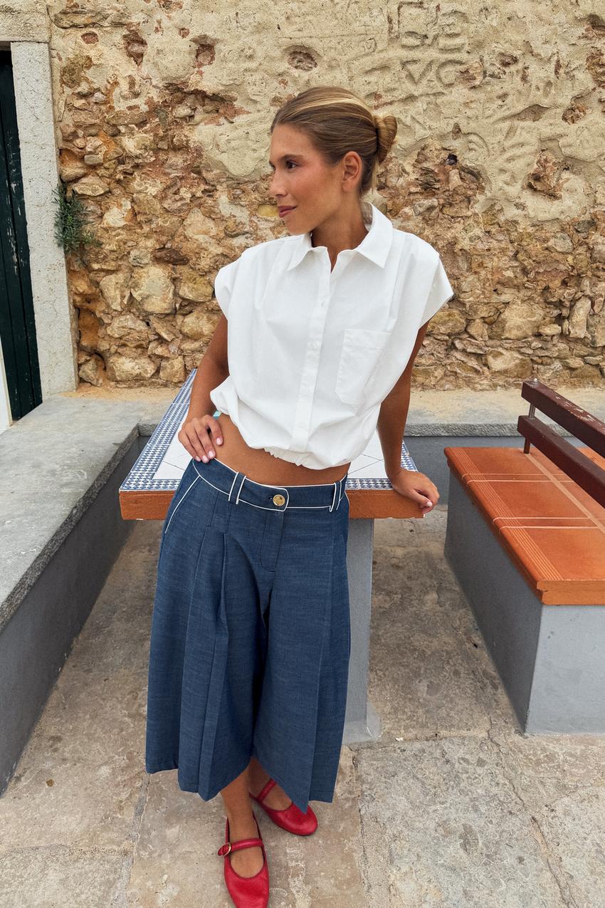 Conjunto de camisa blanca de manga corta con bolsillo, bermuda azul ancha con pinzas, pespuntes blancos y bolsillos laterales, y zapatos rojos.