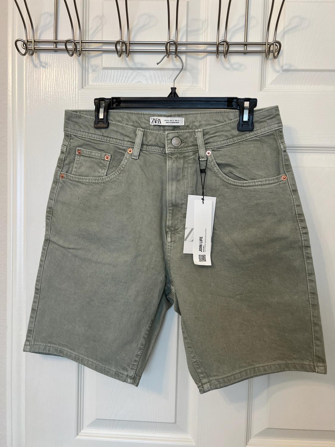 Olive-green denim shorts hanging on a white door. Text: ZARA, Z, JOIN LIFE.
