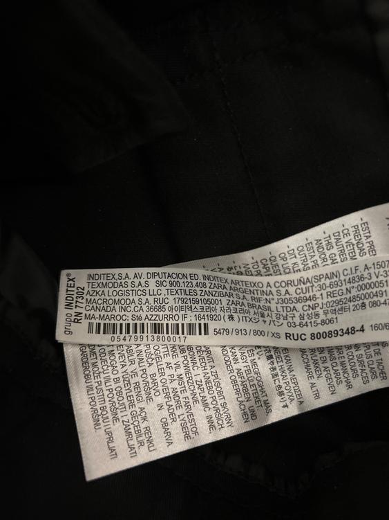 Clothing label with multi-language text, including Inditex manufacturing and distribution information, on black fabric.