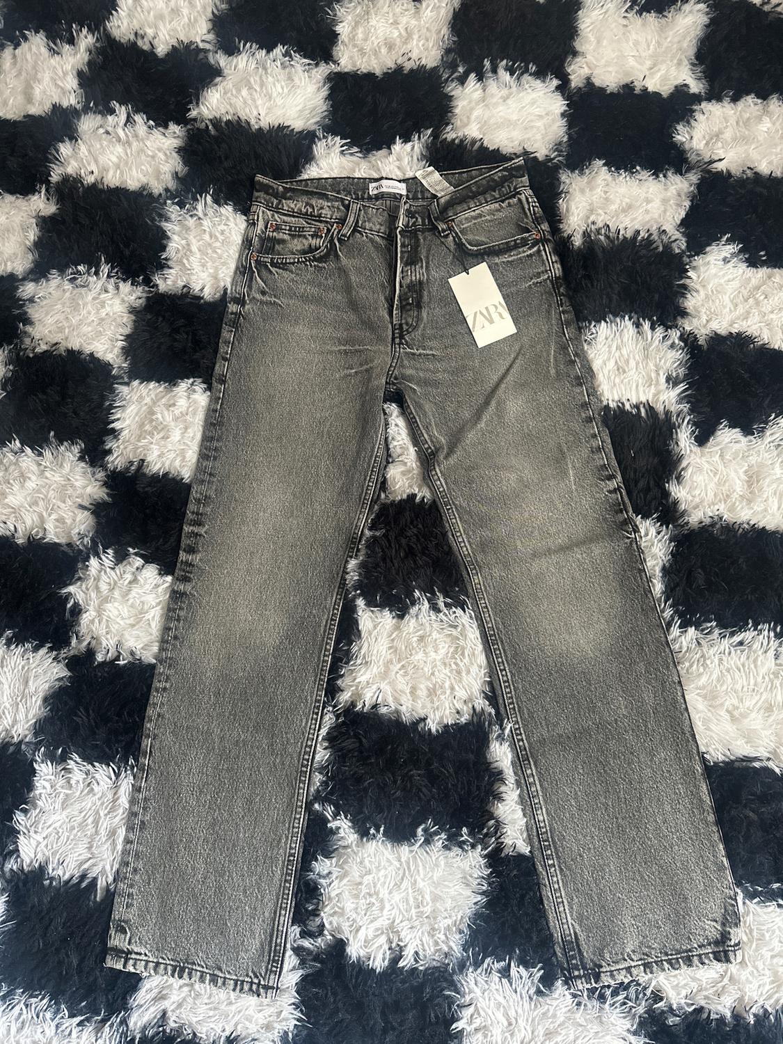 Grey jeans with Zara label on a black and white checked shaggy rug.