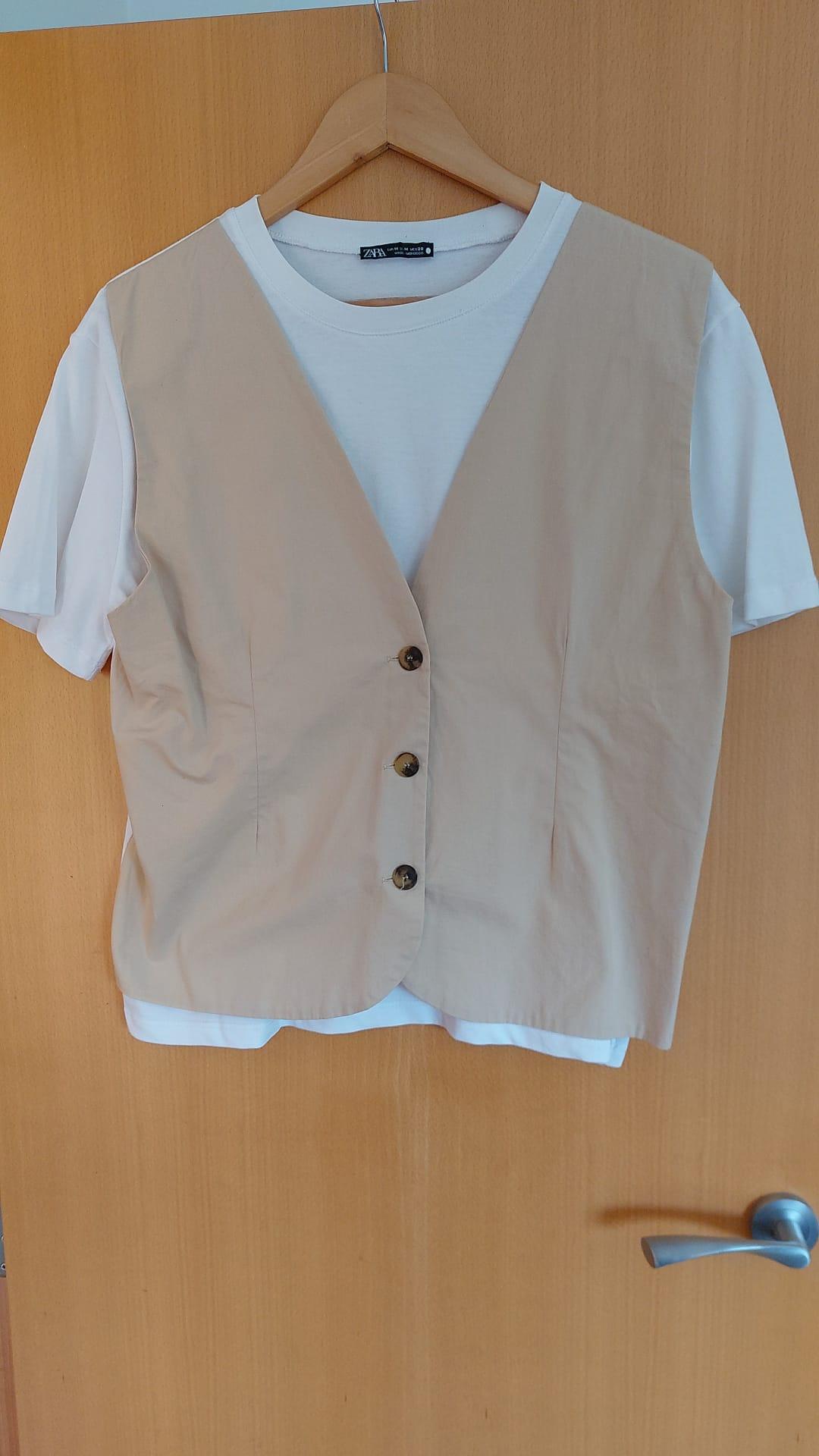Beige waistcoat with buttons over a white t-shirt, hanging on a wooden hanger in front of a light wooden door.