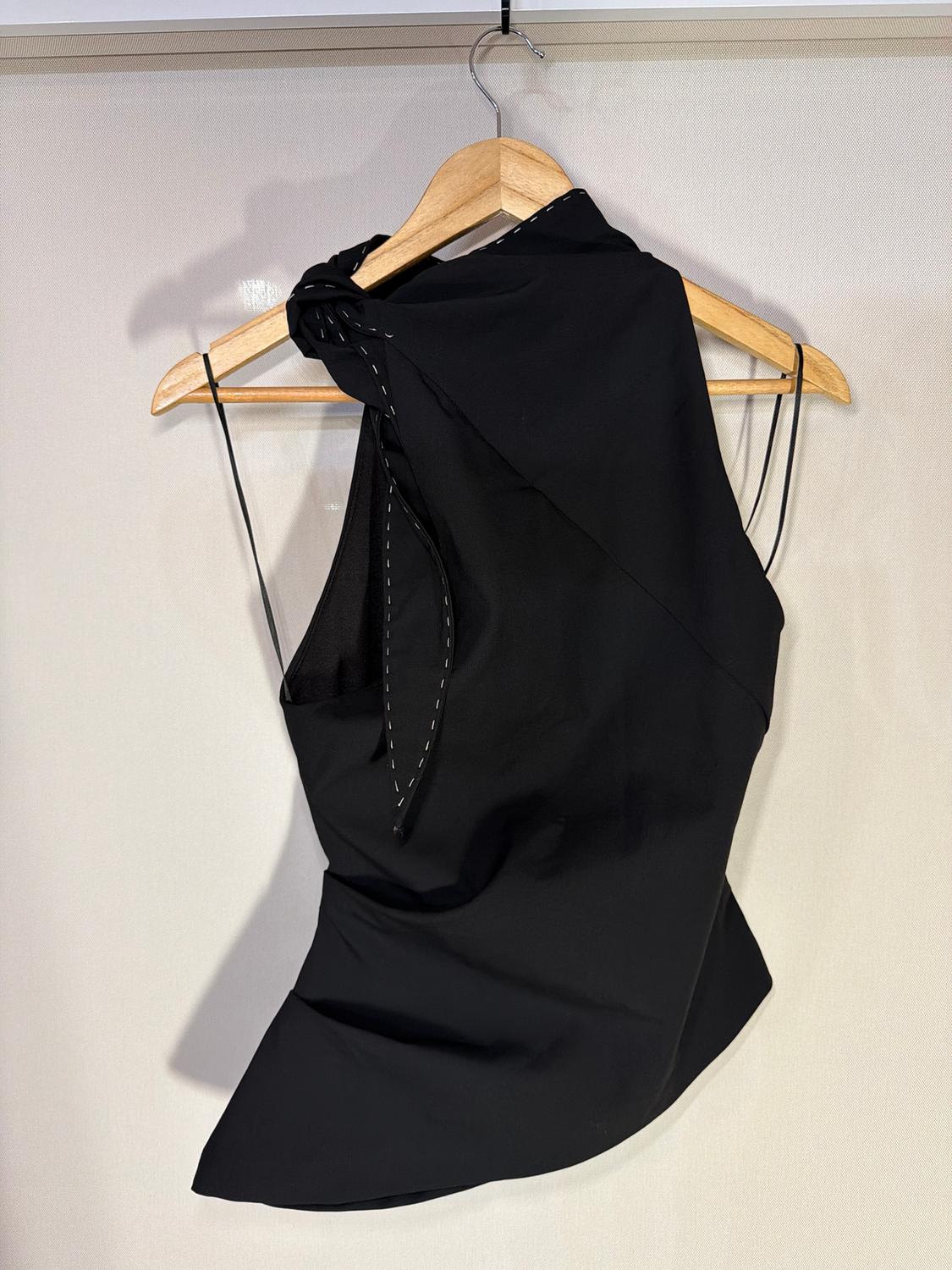 Black sleeveless blouse with a bow at the neck, hanging on a wooden hanger against a light background.