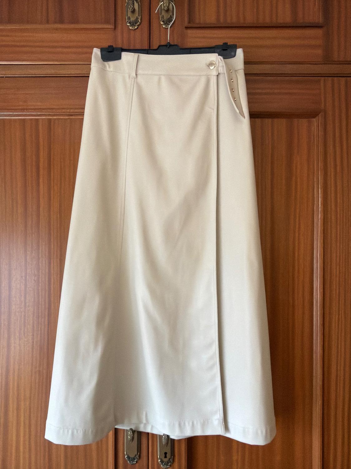 Beige skirt hanging on a black hanger in front of a wooden wardrobe. Simple design with a decorative button at the waist.