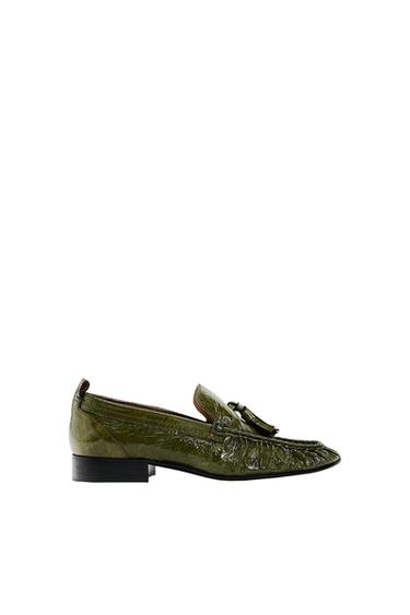 Olive green loafers with tassels, black sole and shiny finish on a white background.