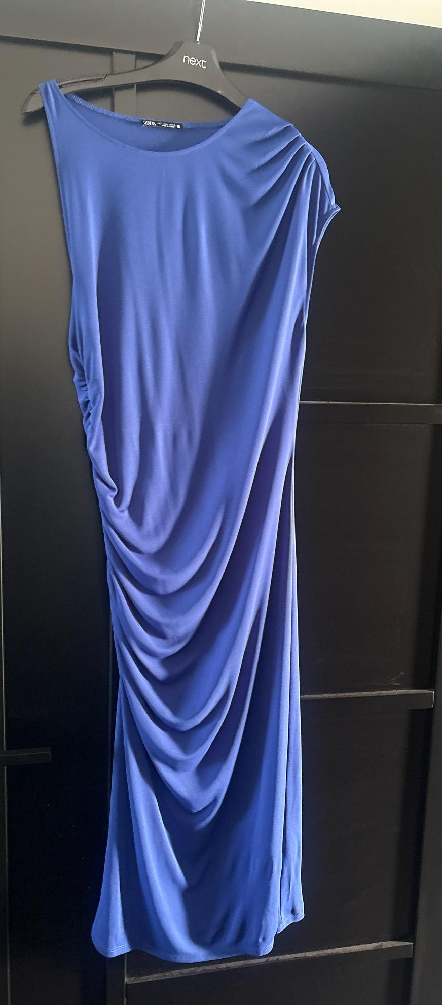 Blue dress with side ruching on a black hanger with the text "next" against a dark background. "ZARA" label visible on the neckline.