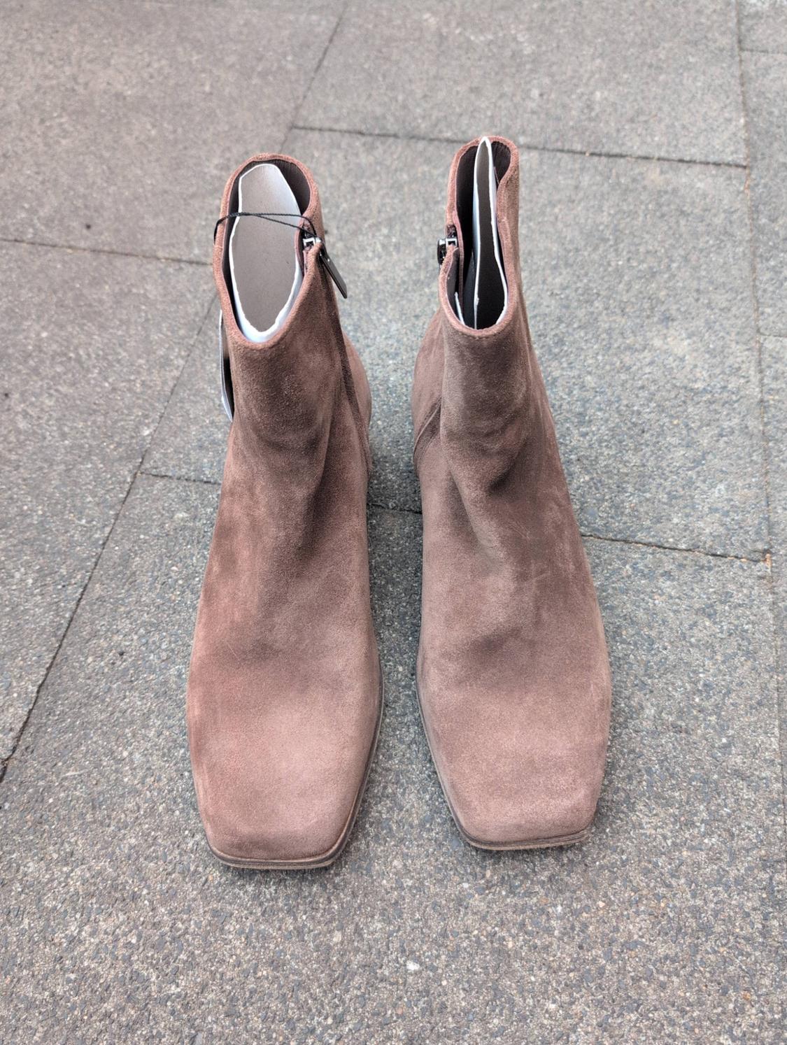 Brown suede ankle boots with a square toe, viewed from above on a grey stone tiled floor in a casual urban setting.
