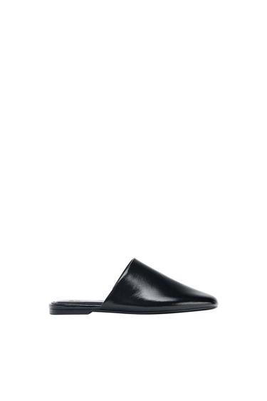 Black closed-toe, open-back shoe on a white background. Minimalist and elegant design.