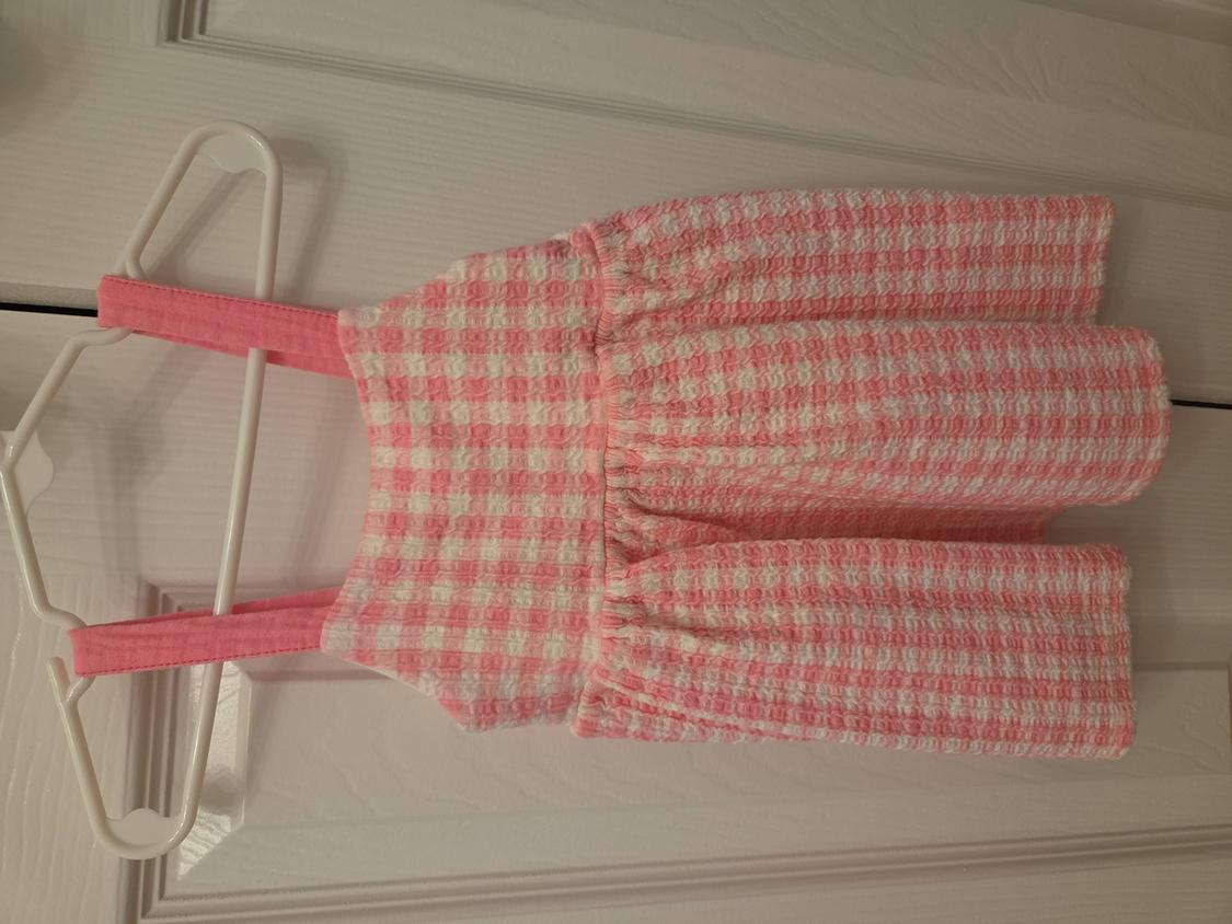 Child's sundress in pink and white tones with a checked print, hanging on a white hanger over a door.