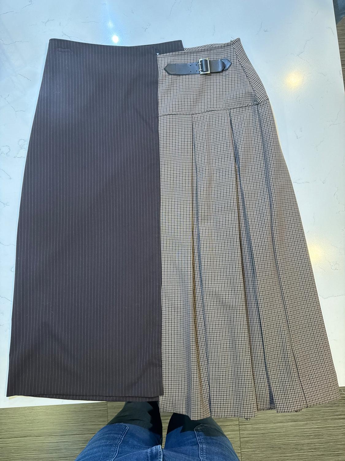 Two-tone midi skirt, half pinstripes and half plaid, with a black belt. White marble background. Person with visible jeans below.