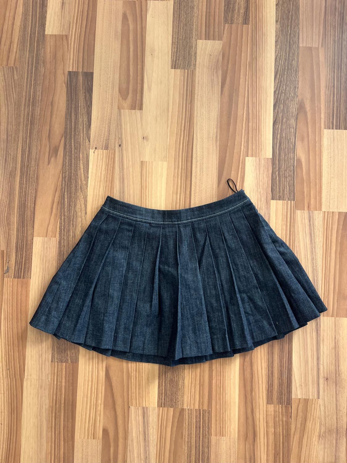 Dark blue denim pleated skirt on a light wooden floor with brown grain.