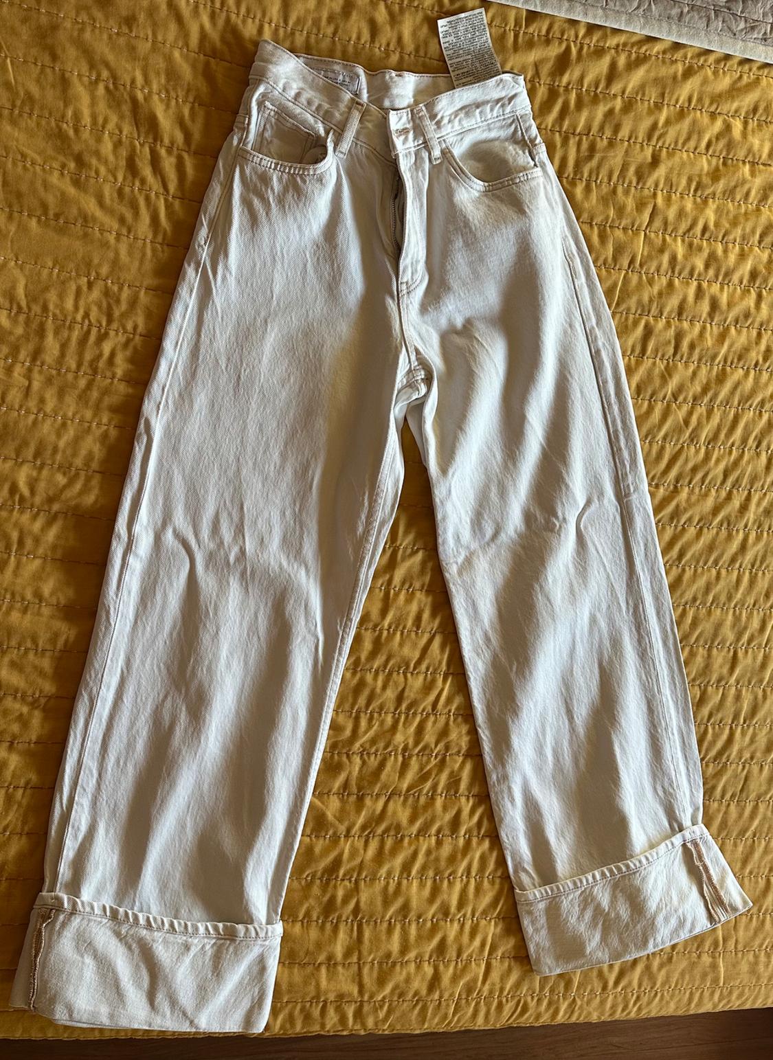 High-waisted, wide-leg white jeans with large hems, laid out on a quilted yellow bedspread.