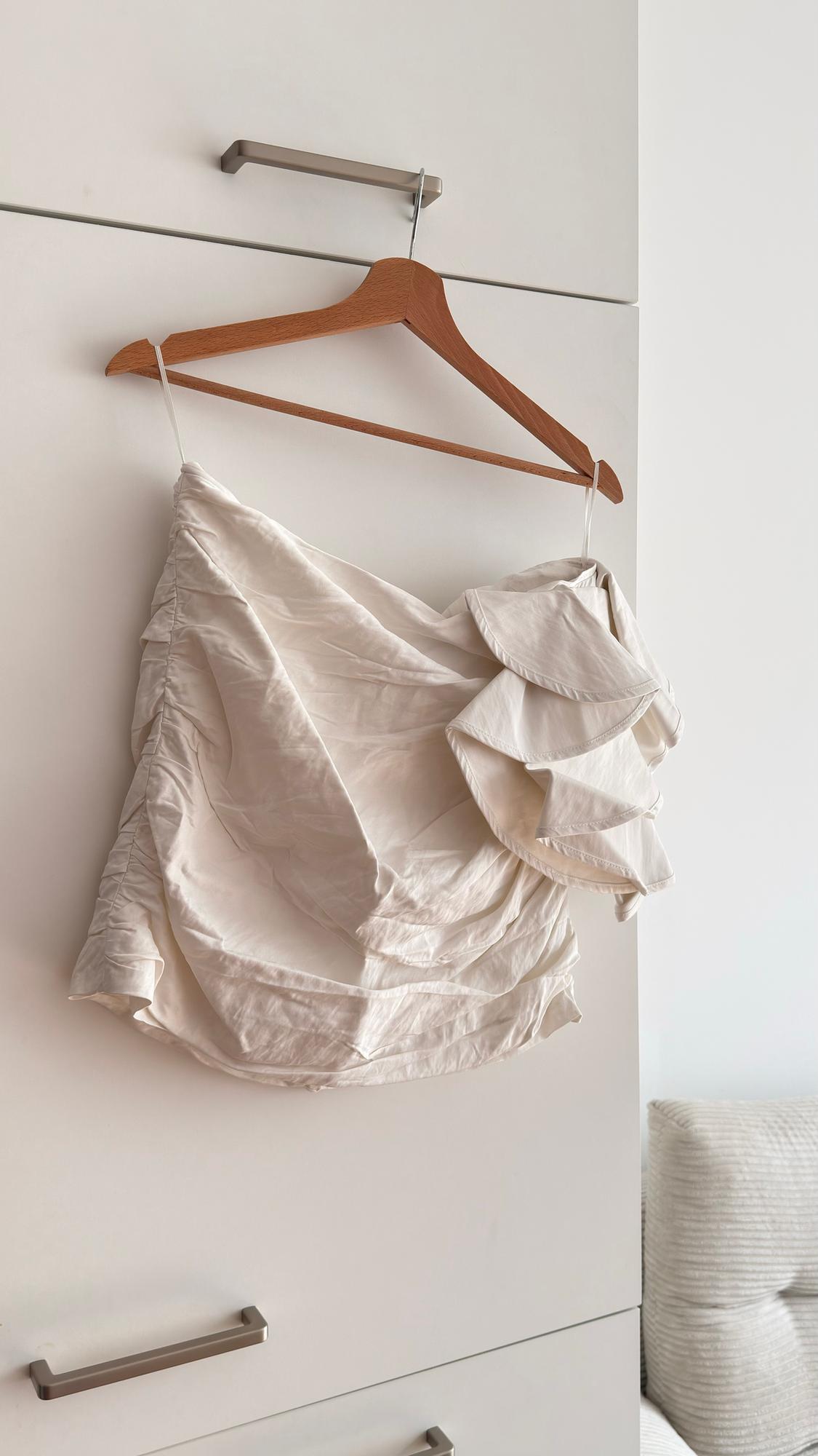 White ruffled blouse hanging on a wooden hanger over a white wardrobe, next to a beige sofa.