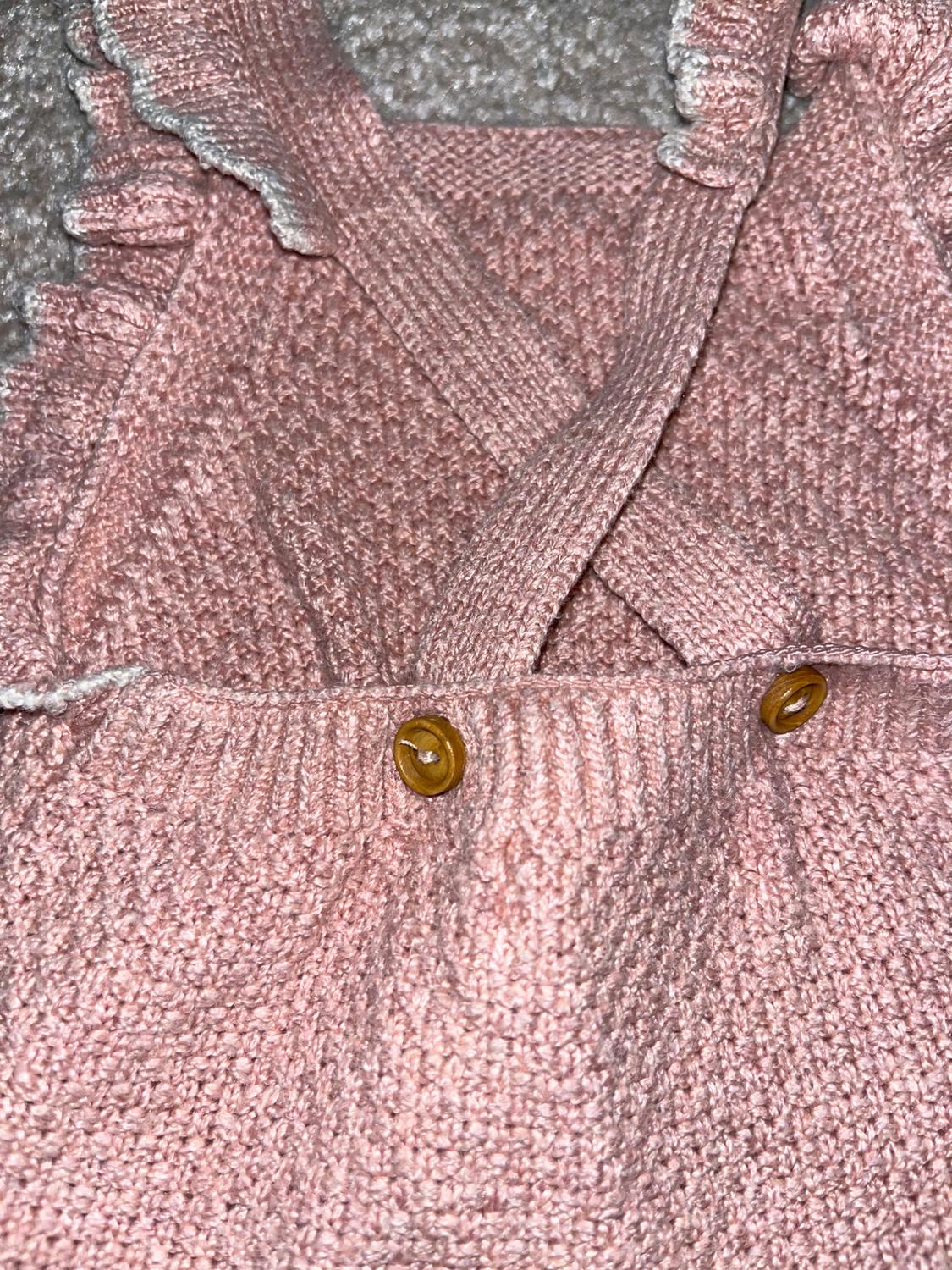 Pink fabric detail with criss-cross straps and brown buttons. The edge has small ruffles. Grey fabric background.
