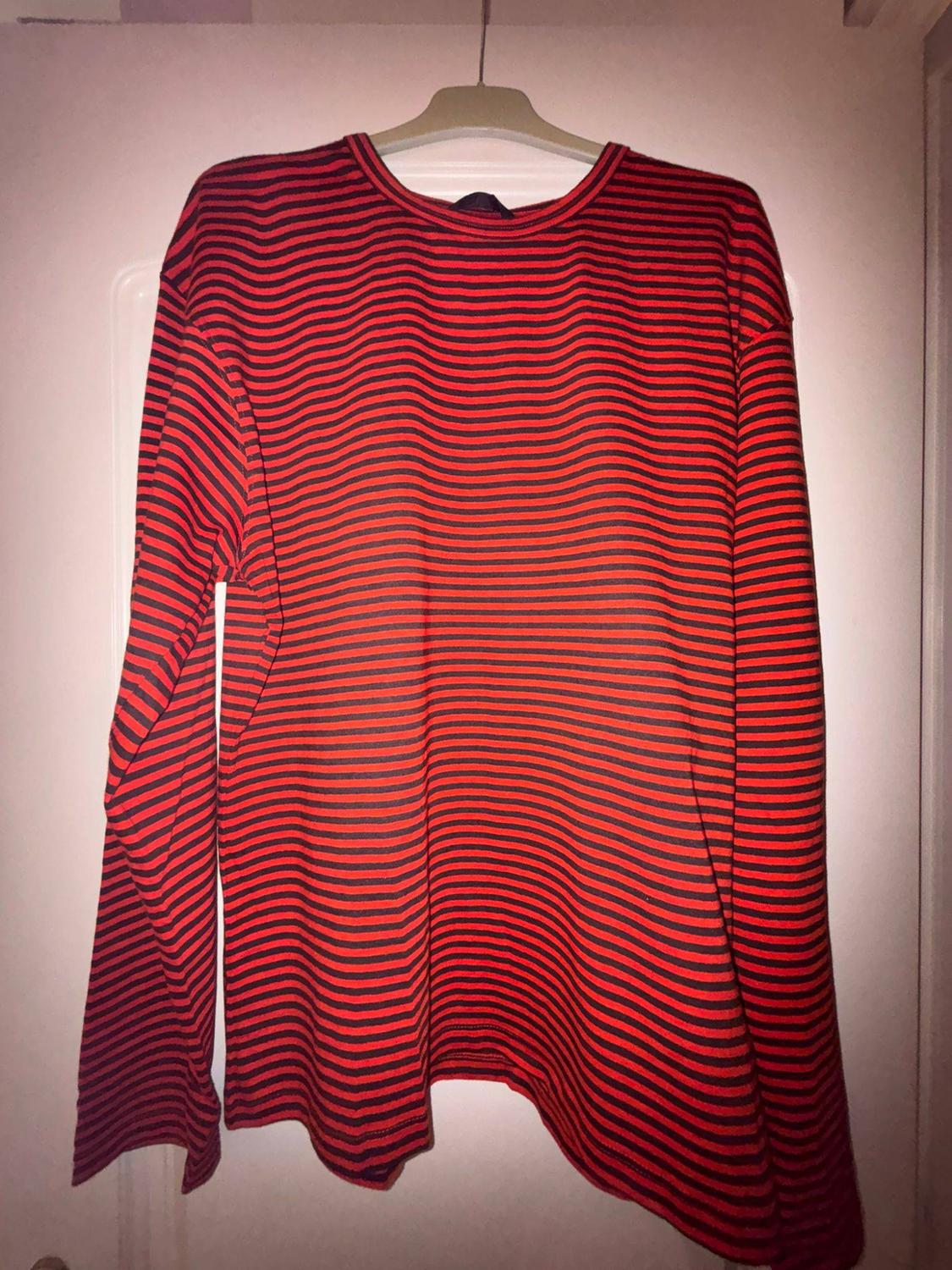Long-sleeved T-shirt with horizontal red and black stripes hanging on a hanger over a white door.