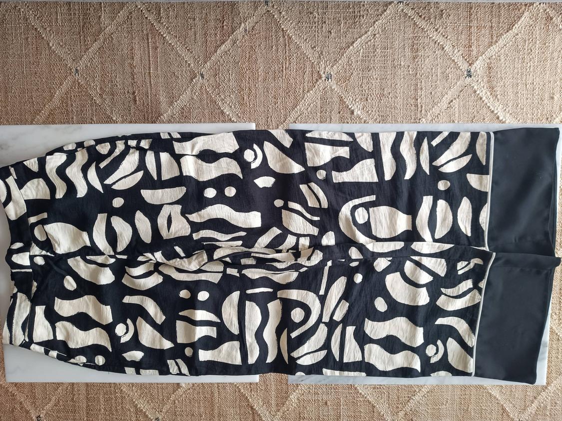 Black trousers with an abstract cream print and plain black hem, on a white surface and a beige rug with a diamond texture.