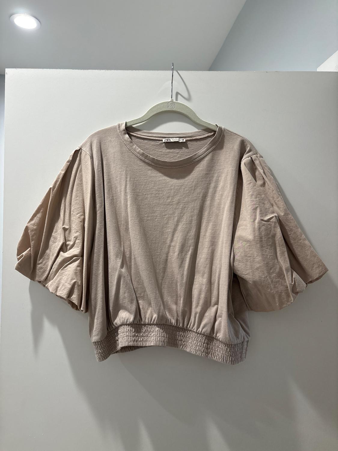 Beige short-sleeve puff-sleeve blouse hanging on a white hanger against a light gray background.