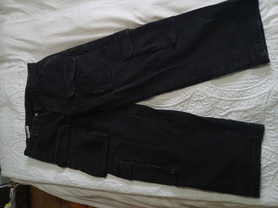 Black shorts with large pockets, placed on a white bedspread with a circular pattern design.