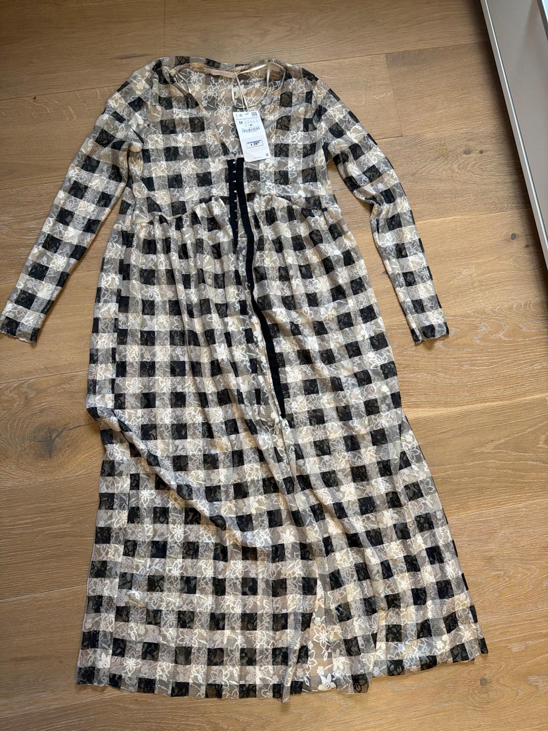 Sheer lace maxi dress with black and beige check print, on a wooden floor. Visible label on the collar.