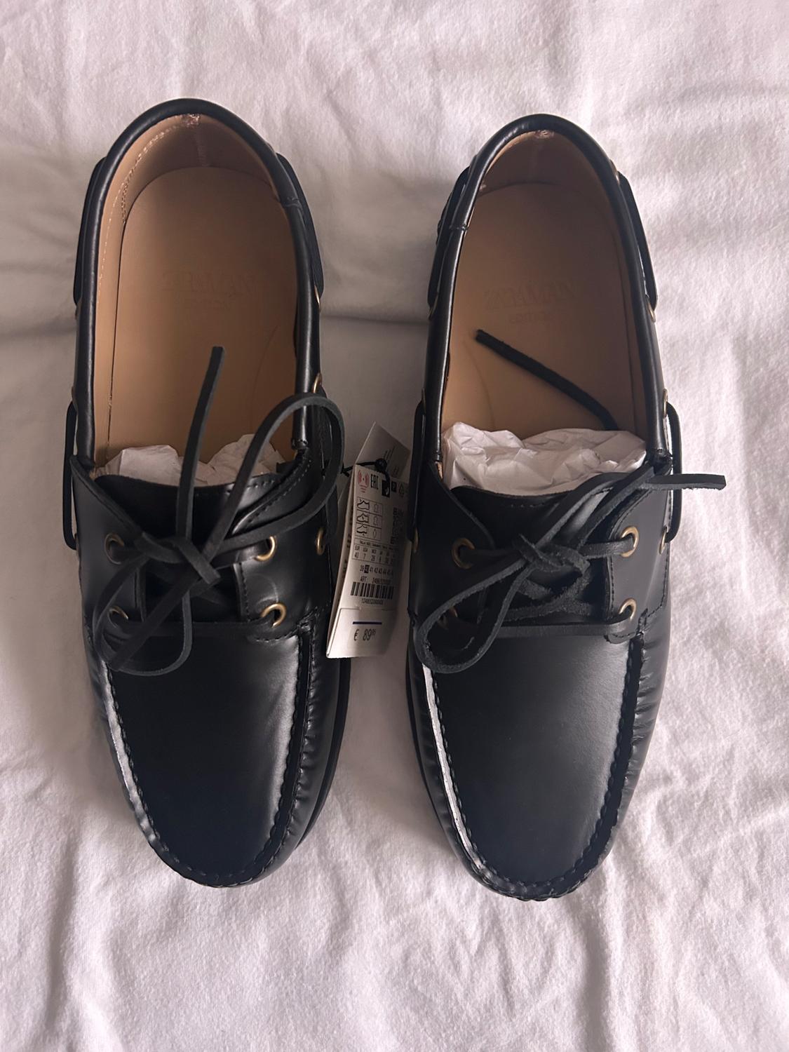 Black leather lace-up shoes on a white surface. Visible tag on the right shoe.