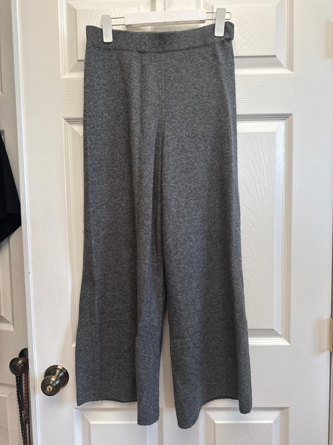 Grey knitted trousers hanging on a white hanger in front of a white panelled door.