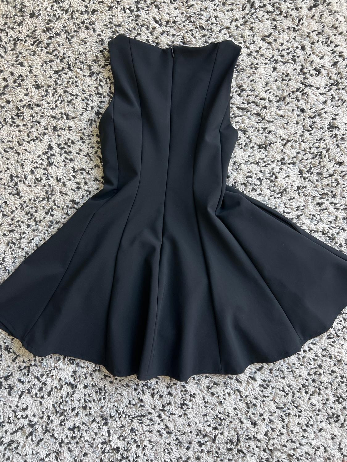 Sleeveless black dress with a flared skirt, laid out on a thick-textured rug in shades of grey and white.