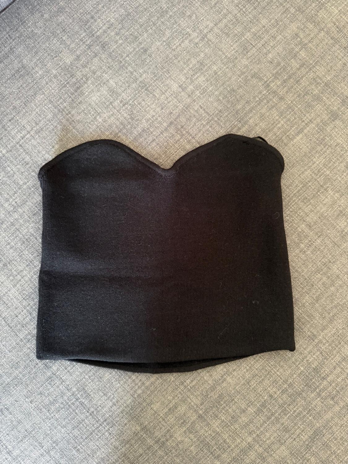 Black strapless top with a sweetheart neckline, made from knitted fabric, against a grey fabric background.