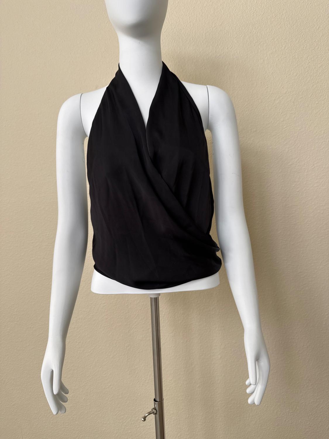 White mannequin wearing a black sleeveless, halter-neck, draped crossover top, in front of a minimalist beige wall.