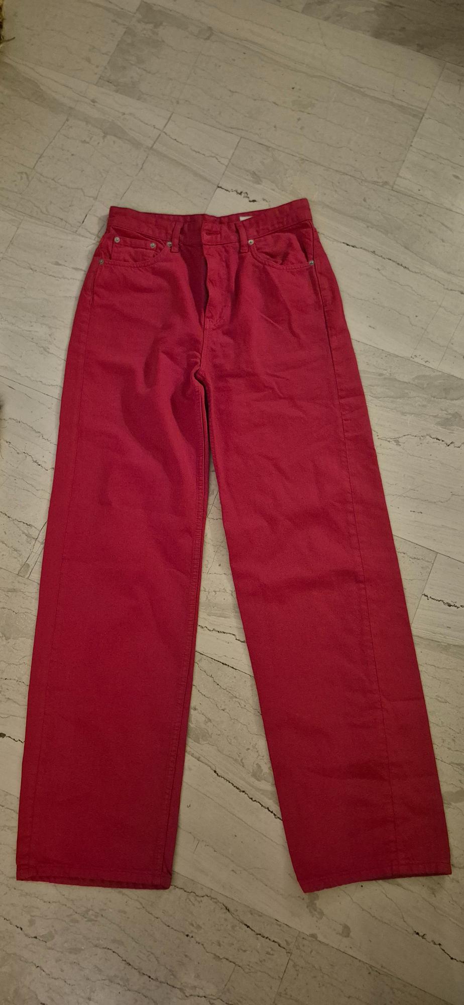 Straight-cut red trousers on a light marble floor. The trousers have front and back pockets.