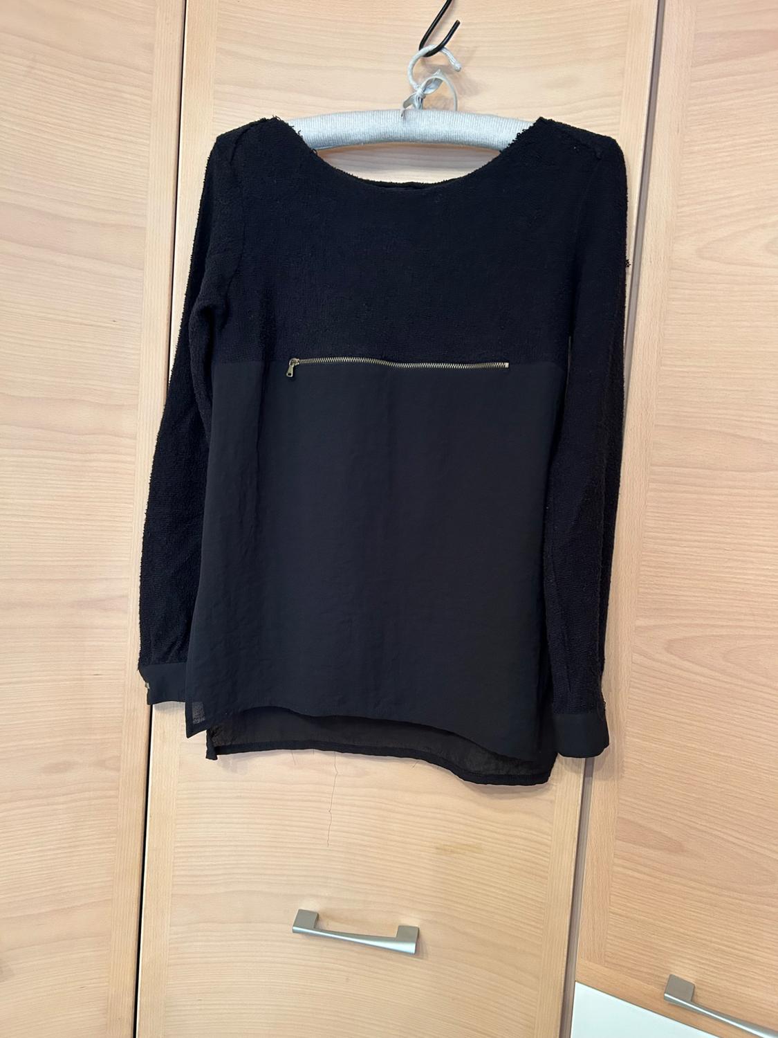 Front view of a black blouse with a chest zip and long sleeves.