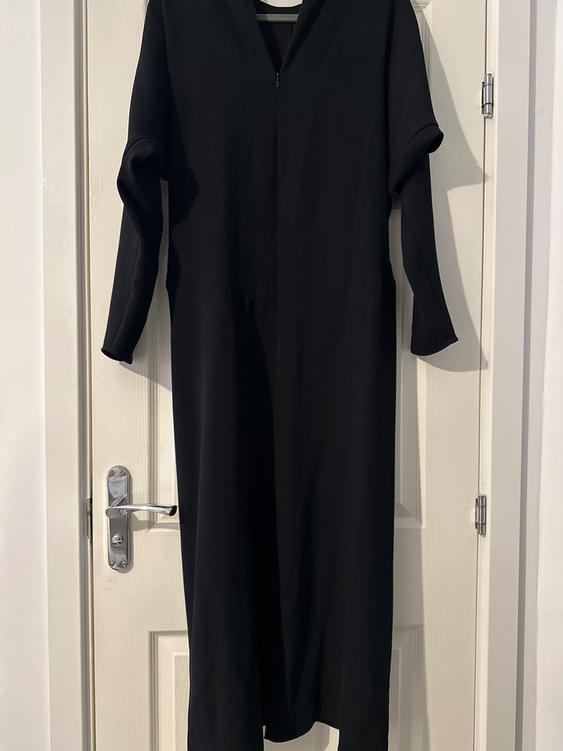 Long-sleeved black dress hanging on a white door. The design is simple and elegant, ideal for formal occasions.
