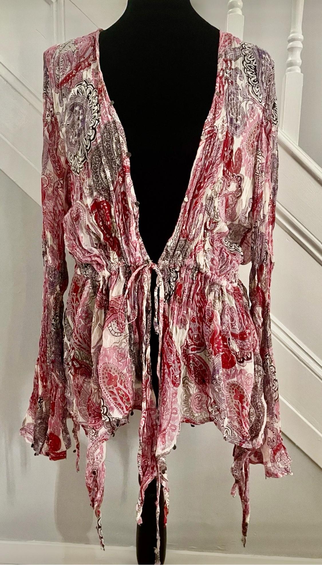 Patterned blouse in red and white tones with a floral design and bows, displayed on a black mannequin in front of a white staircase.