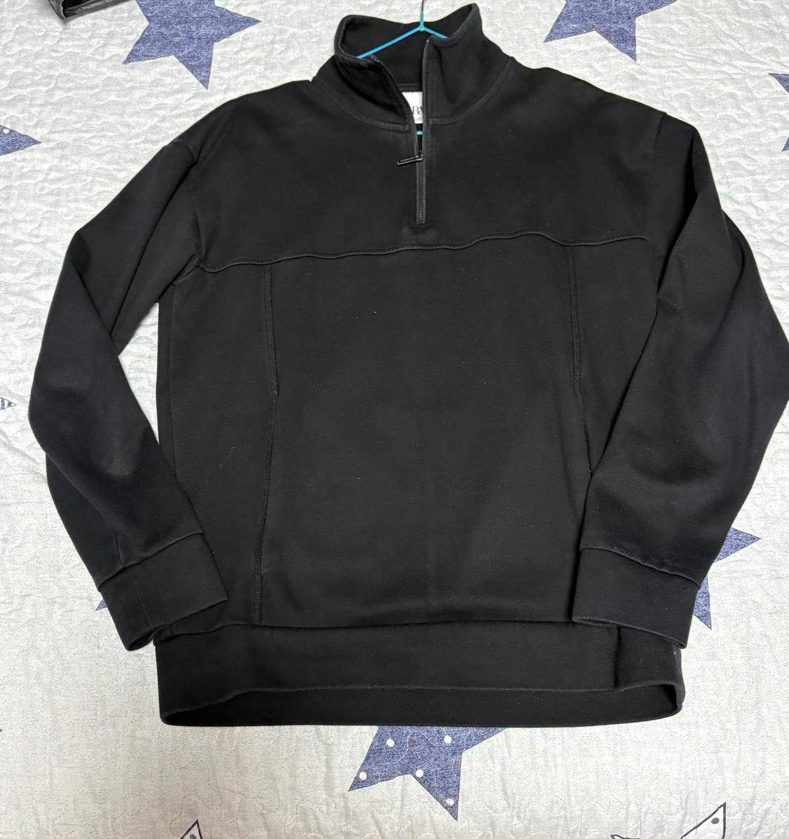 Black high-neck sweatshirt with a half zip and decorative stitching, on a light background with a blue star print.