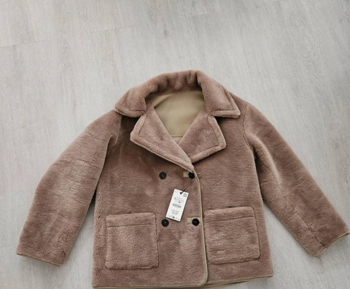 Light brown soft-textured jacket with lapels, dark buttons and front pockets, laid out on a wooden floor.