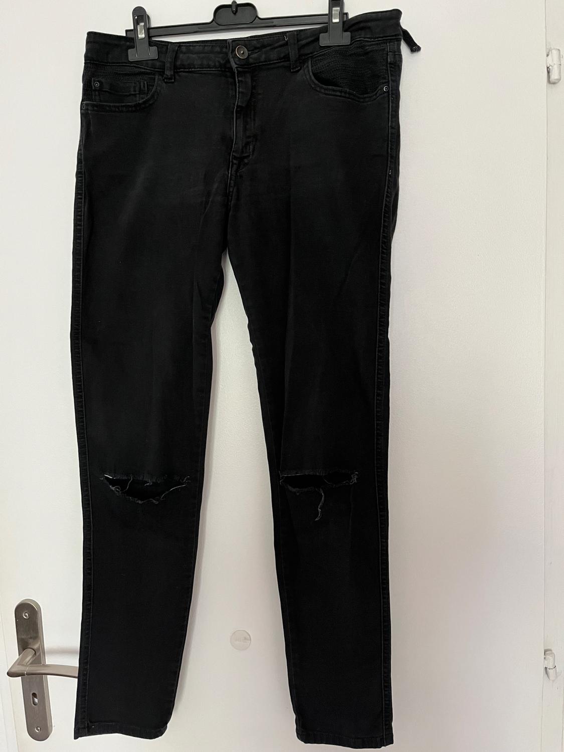 Front view of black trousers with ripped knees and five pockets.