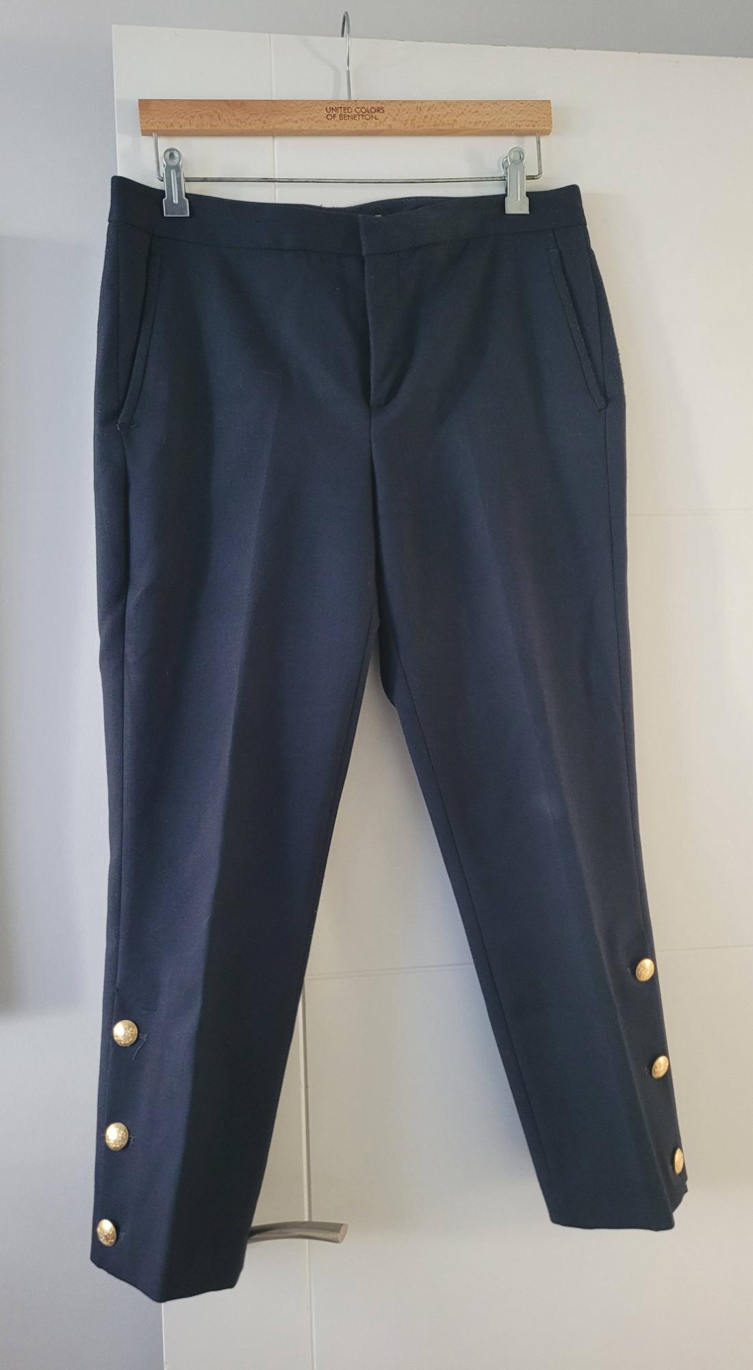 Dark blue trousers hanging on a wooden hanger with gold buttons on the cuffs. Visible text: "UNITED COLORS OF BENETTON".