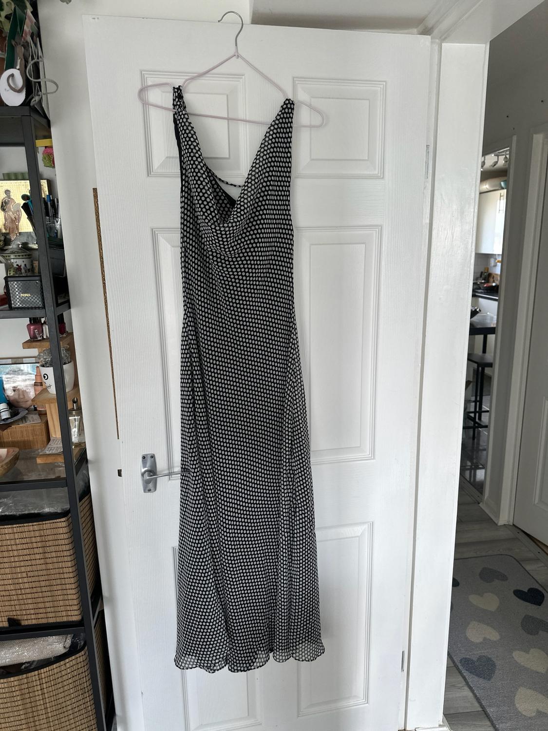 Black and white polka dot maxi dress hanging on a white door in a house. Visible text: FOSSIL.