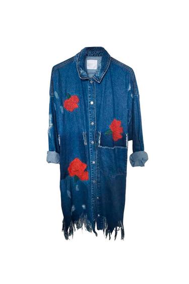Long casual denim shirt with embroidered red roses, distressed details, rolled-up sleeves and a frayed hem on a white background.