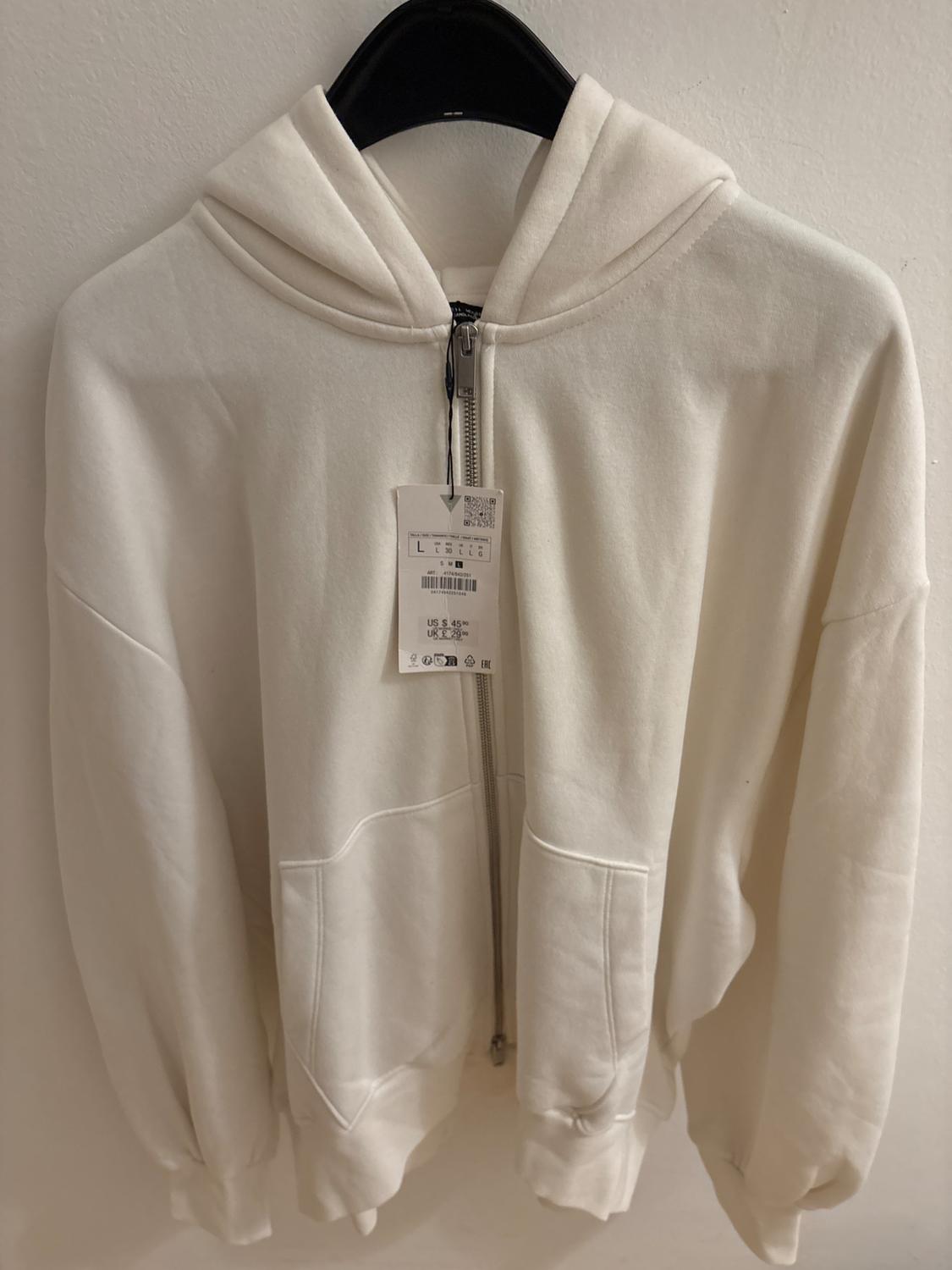 White hooded zip-up sweatshirt hanging on a black hanger. Visible tag with size and price details.