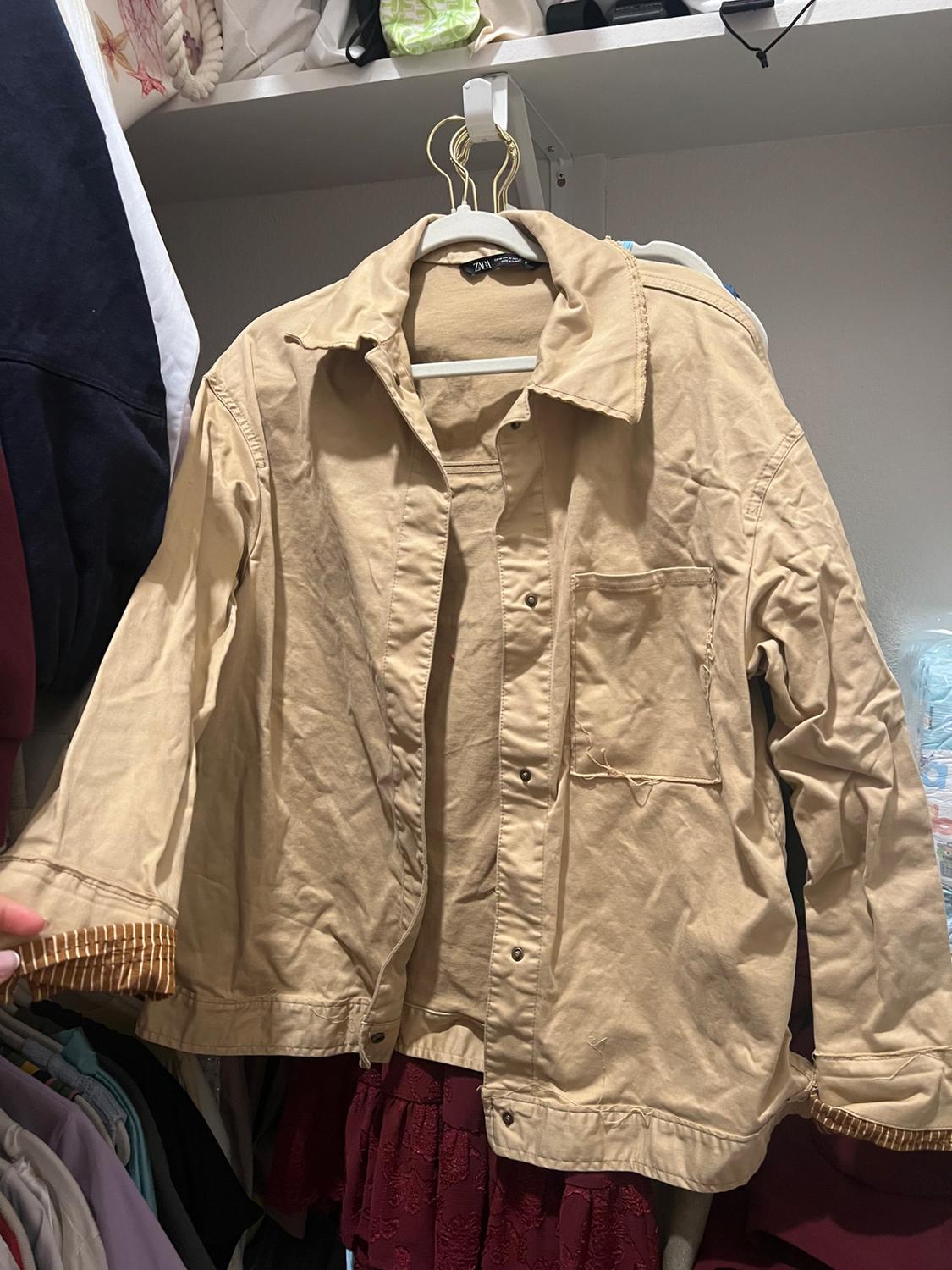 Front view of beige jacket with front pockets and snap buttons.