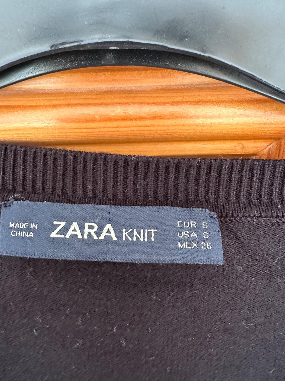 Detail of label on black garment with text 'ZARA KNIT', 'MADE IN CHINA', 'EUR S', 'USA S', 'MEX 26'.