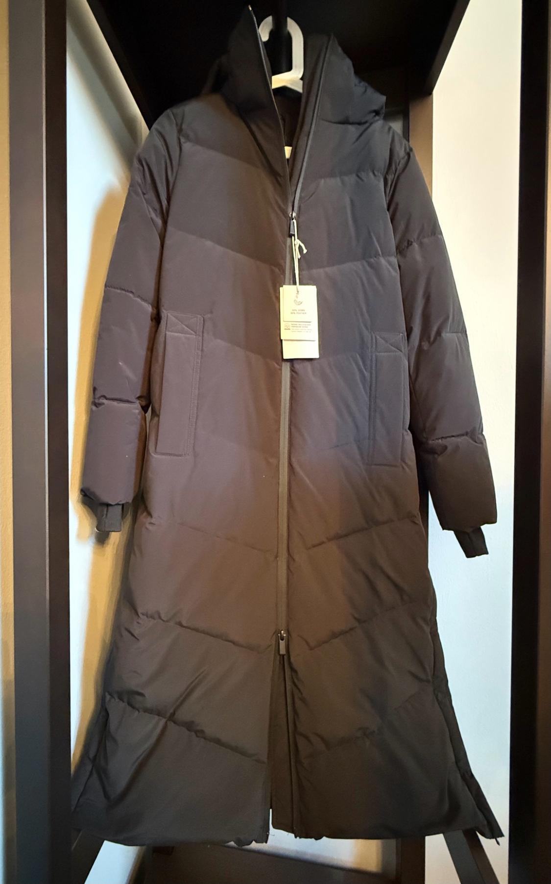 Dark gray quilted long coat with a hood, front zipper closure, and a hanging tag, hung on a hanger.