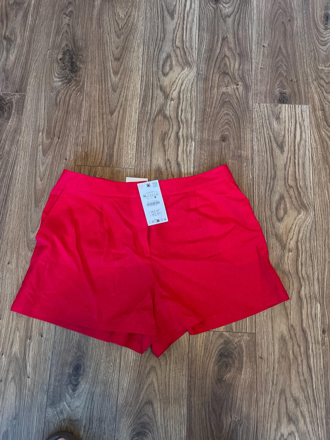 Red shorts laid out on a wooden floor. The waistband features a label with the text XL.